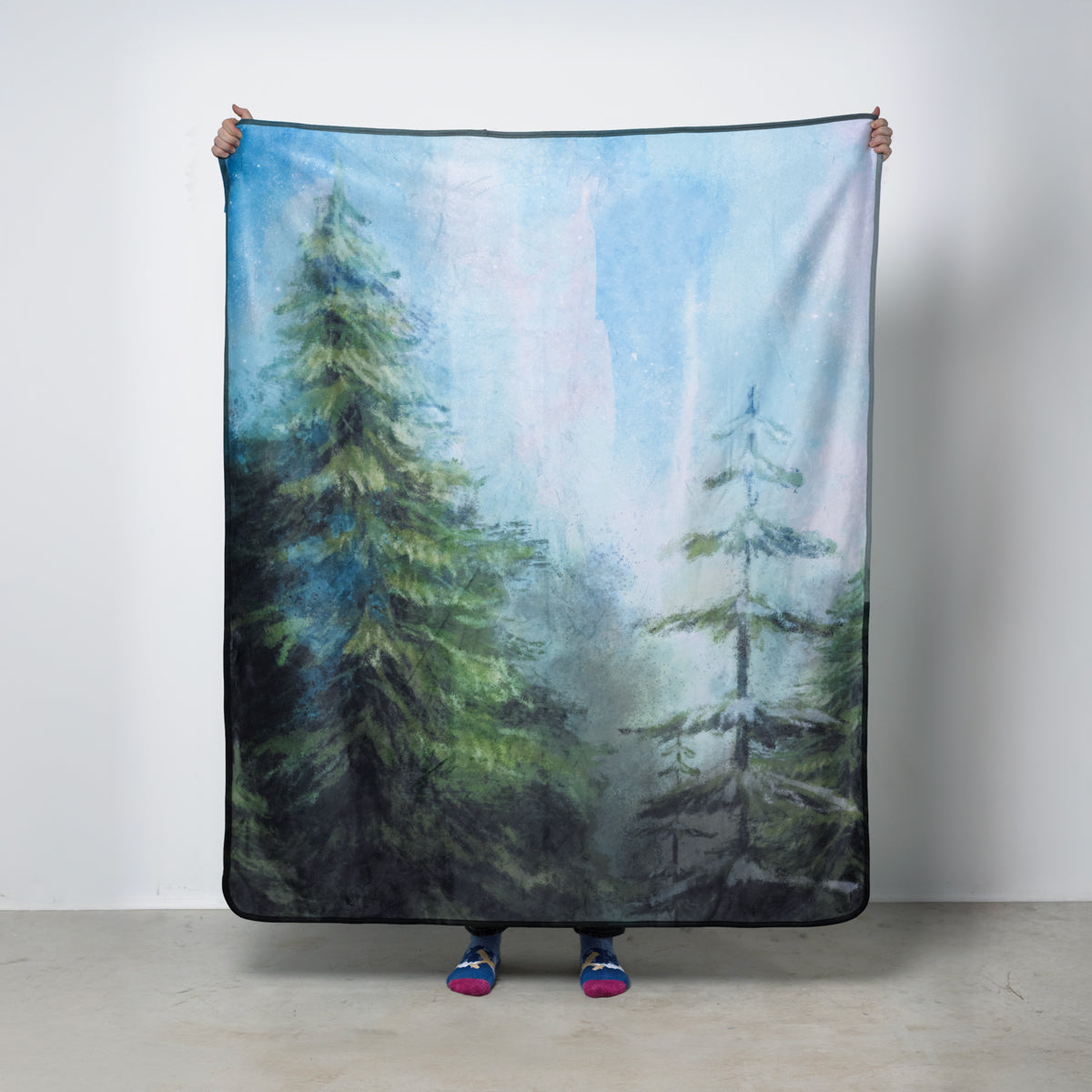 Fleece blanket with an illustrated forest scene and northern lights