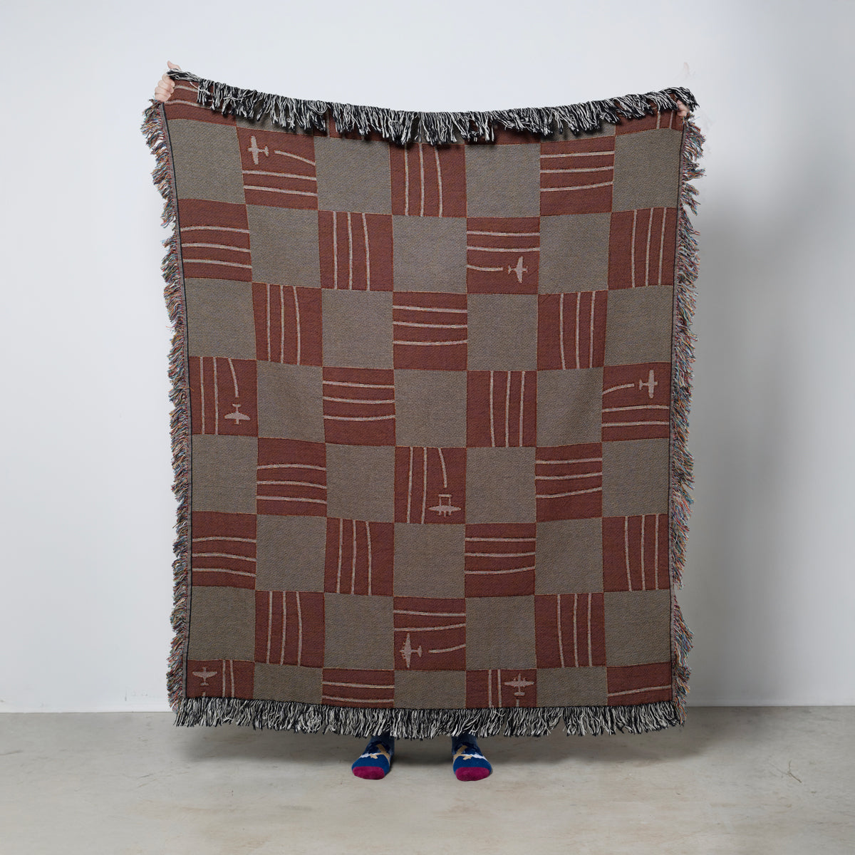 Checkered woven blanket with fringes and airplanes in rich warm tones