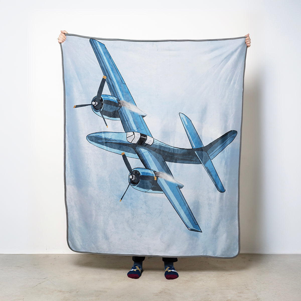 Fleece blanket with a vintage Grumman F7F Tigercat airplane design against a light blue sky background