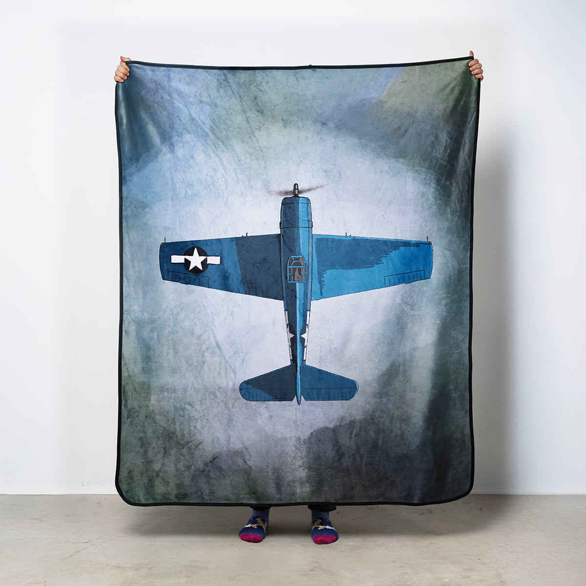 Person holding a Grumman F6F Hellcat blanket against a blue green background