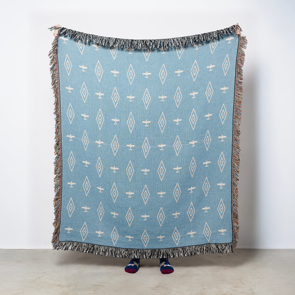 Blue airplane and diamond patterned throw blanket with fringe on a blue background