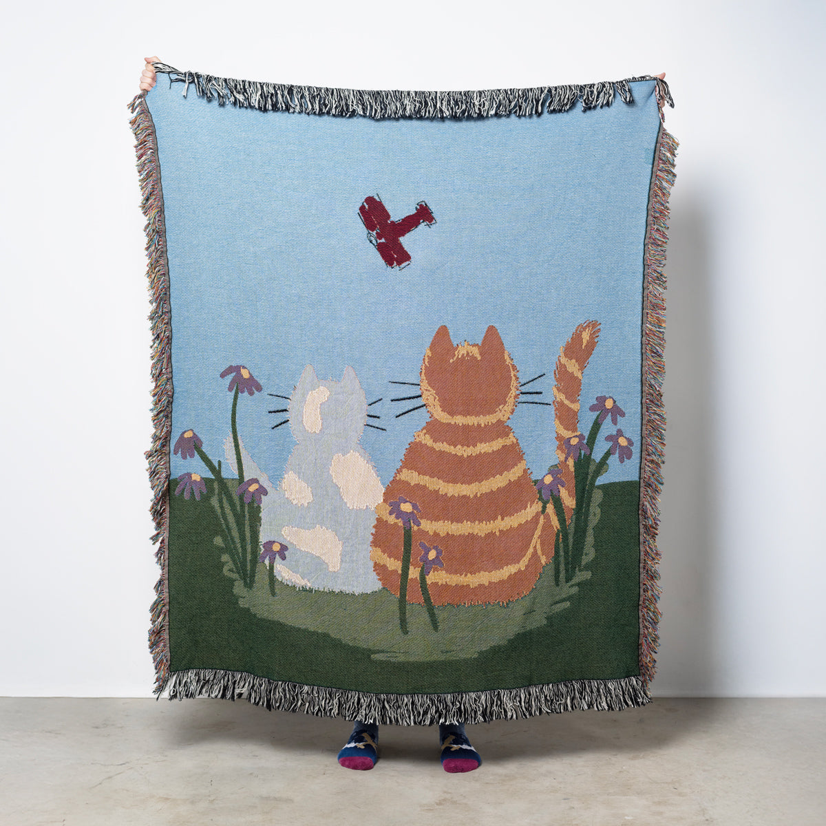 Woven blanket with two cats watching an airplane in the sky