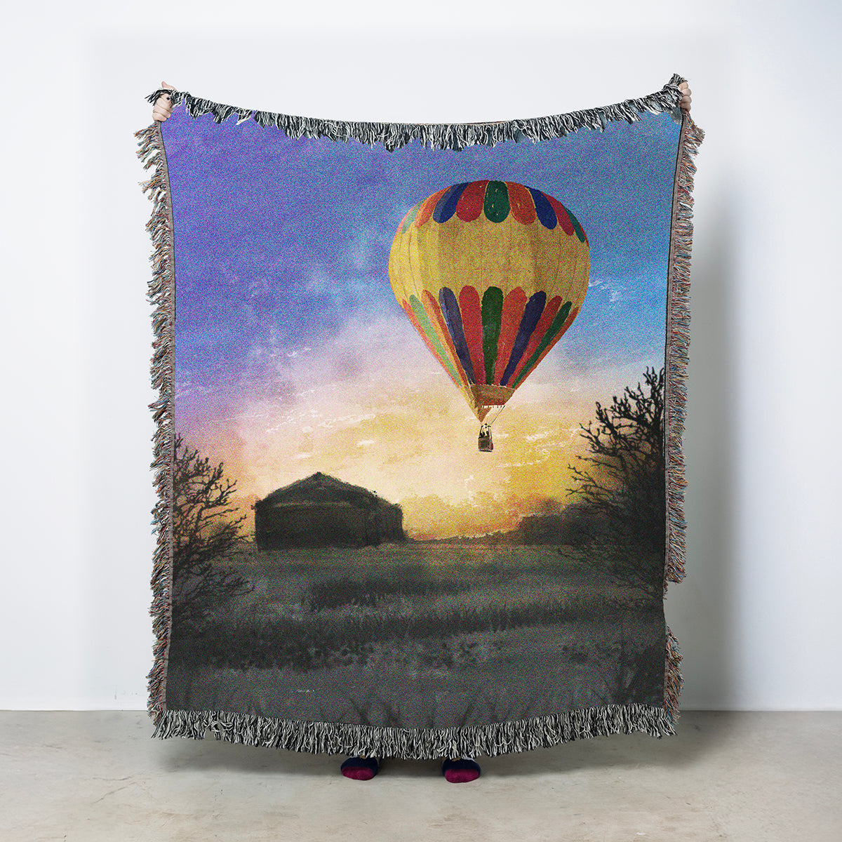 Woven throw blanket featuring a hot air balloon flying over fields with a sunrise