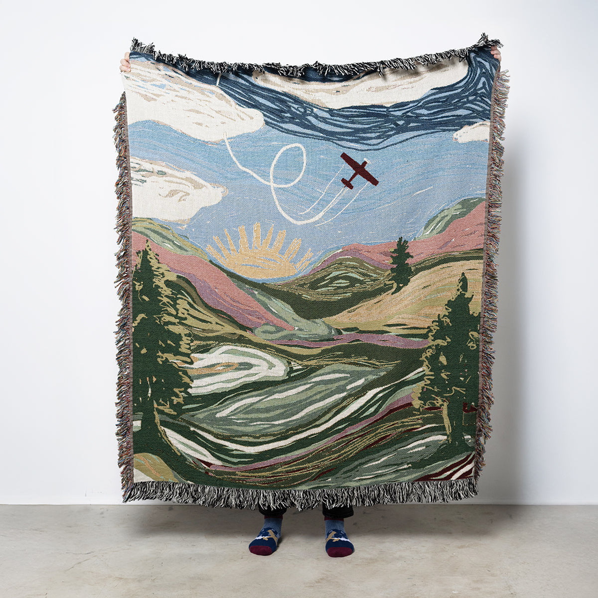 Blanket with an illustrated landscape design featuring a plane, mountains, and trees
