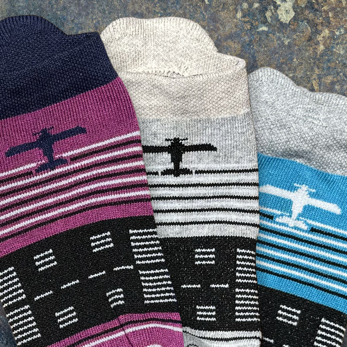 Three pairs of eco performance athletic socks with airplane designs on a textured surface