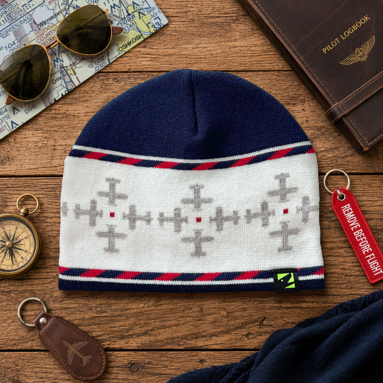 Knitted beanie with airplane pattern on a wooden surface with sunglasses, passport, and compass.