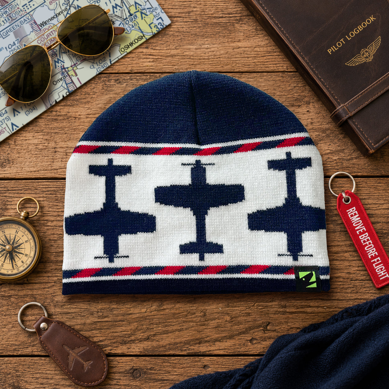 Navy knit beanie with airplane pattern on a wooden surface with accessories.