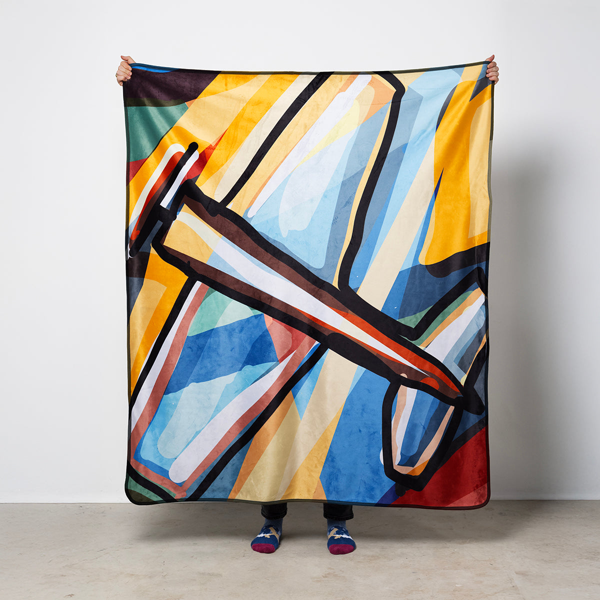 Person holding a colorful abstract patterned blanket against a plain background