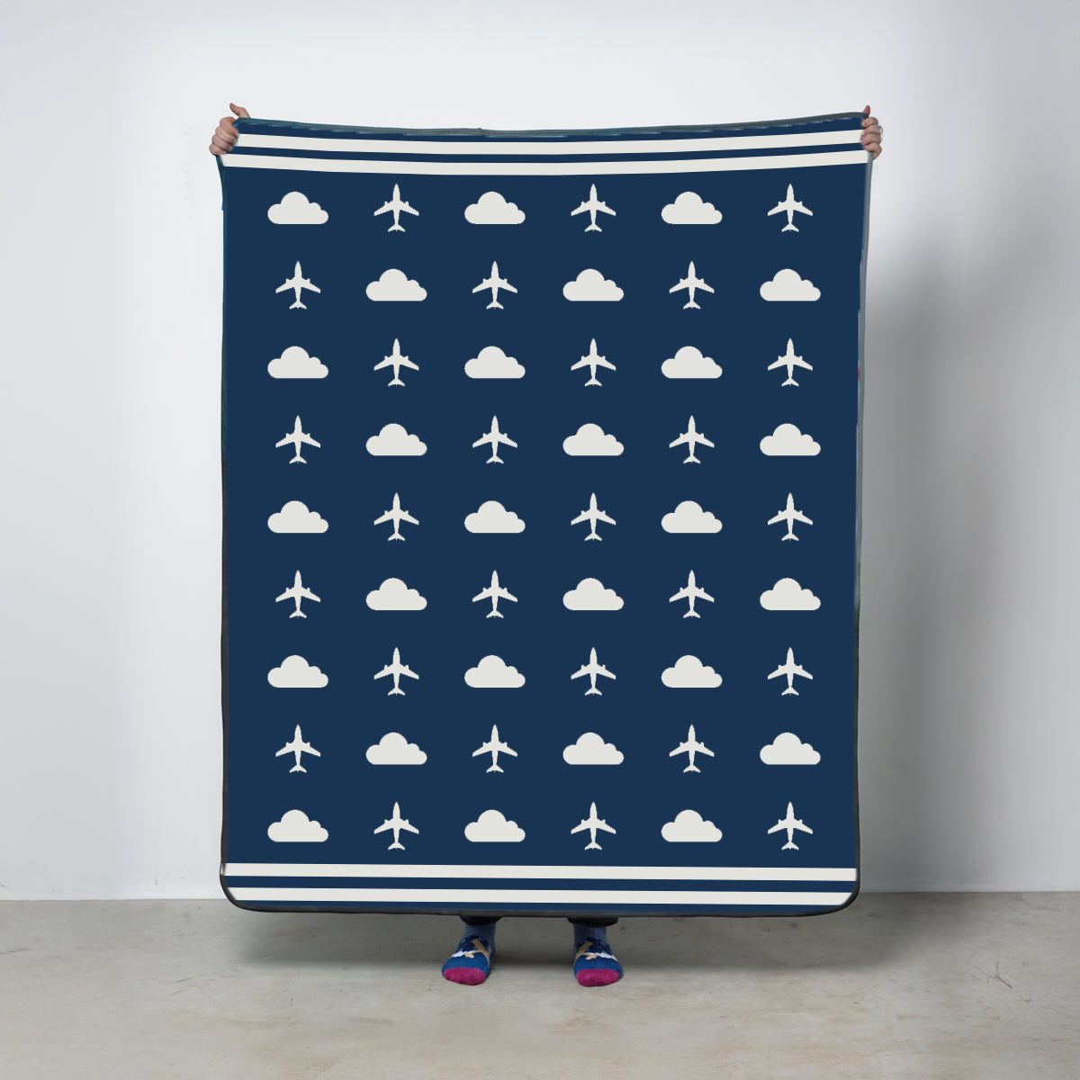 Fleece travel blanket with white airplane and cloud pattern in blue held by a person against a plain background