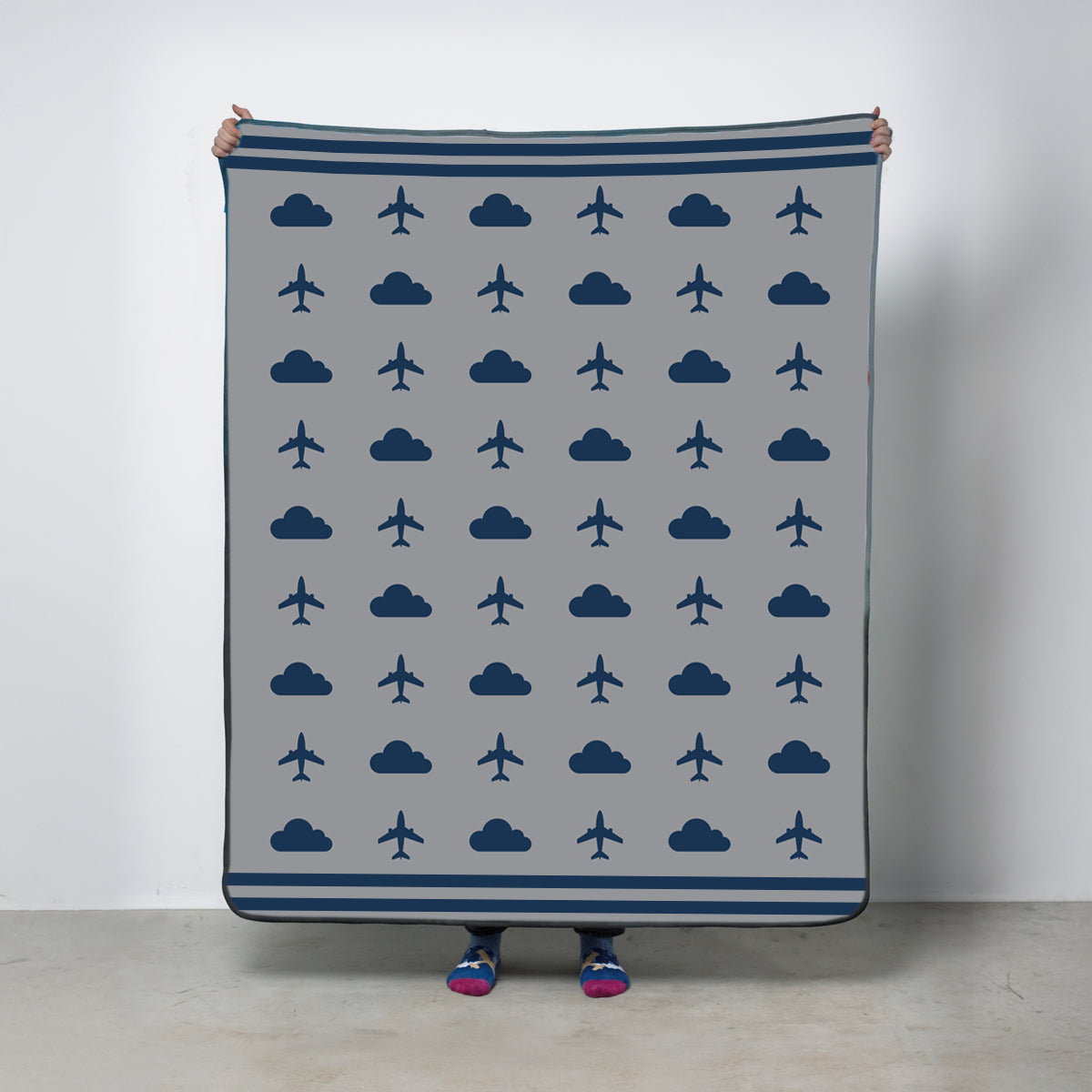 Fleece travel blanket with airplane and cloud pattern on a gray background