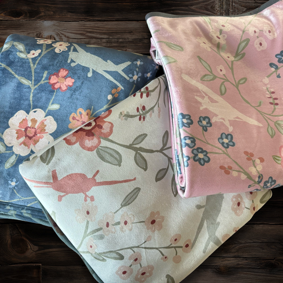 Floral folded blankets with airplanes and flowers in pink, cream, blue on a wood background