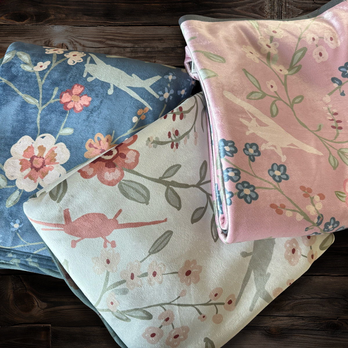 Floral folded blankets with airplanes and flowers in pink, cream, blue on a wood background