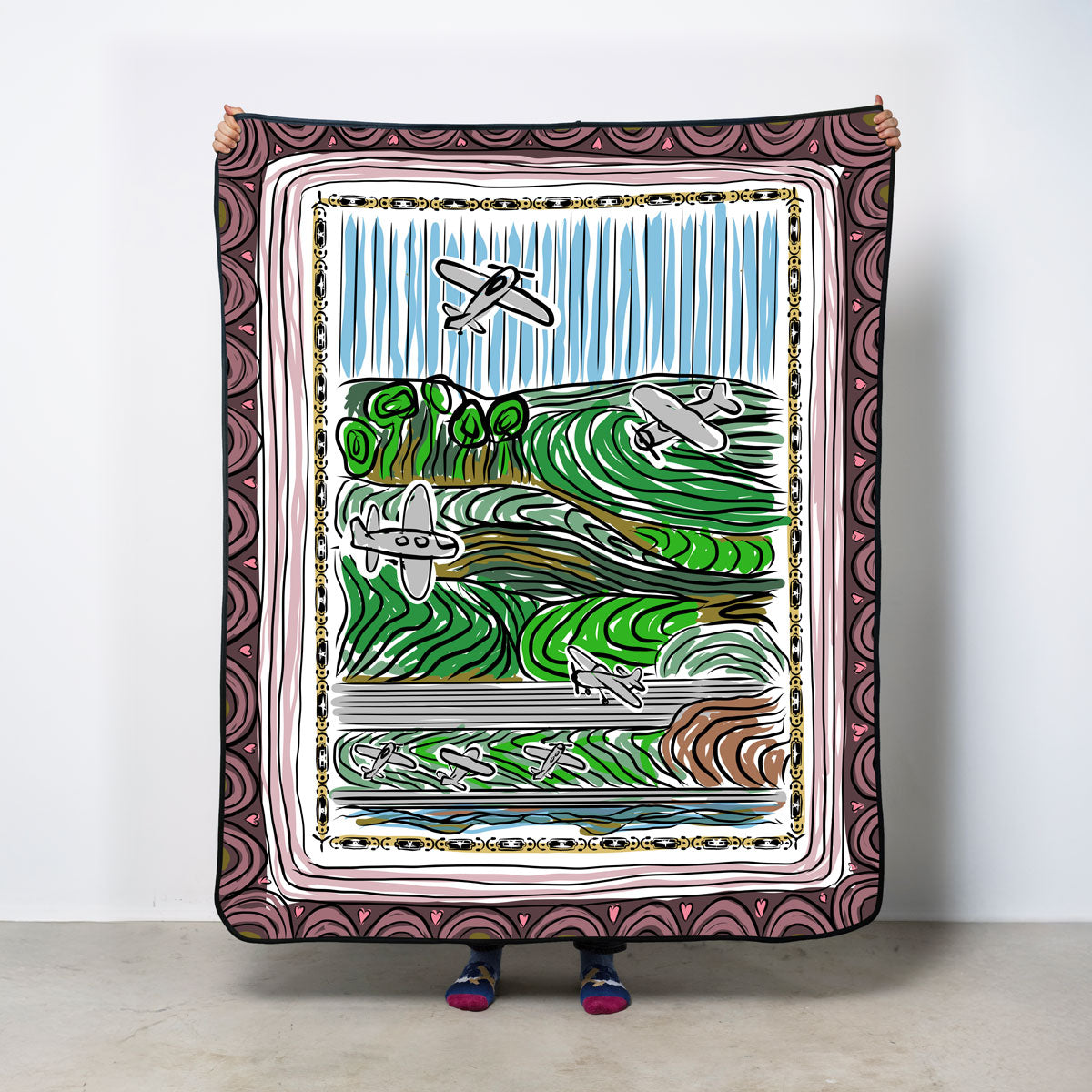 Person holding a decorative blanket with a scenic design and airplanes illustration.