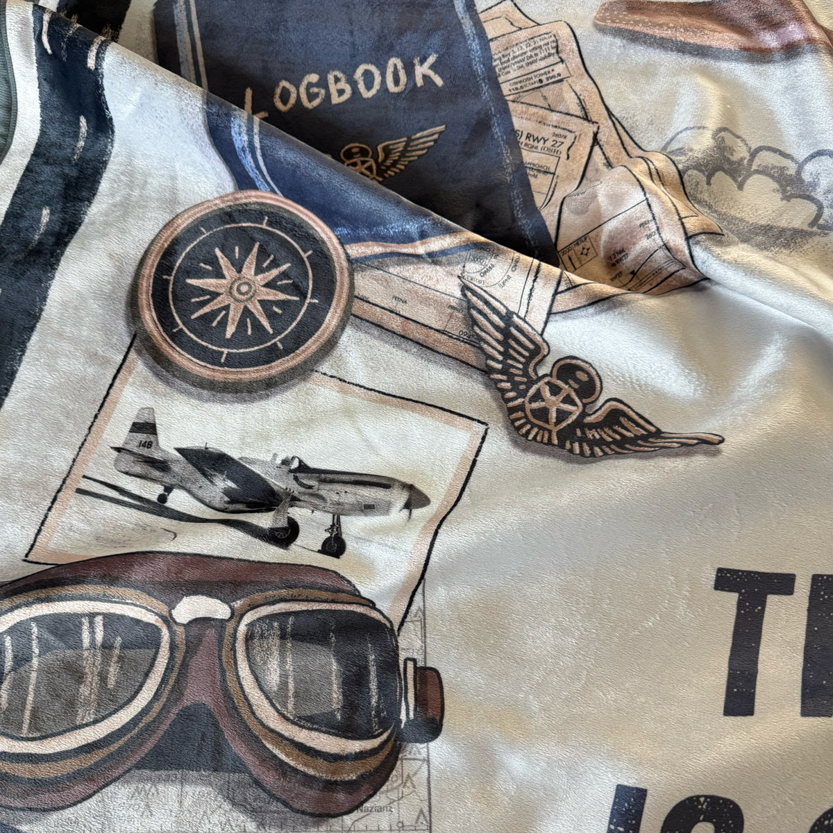 Close-up of a blanket with aviation-themed designs including goggles, airplane, compass, P-51 Mustang, and text.