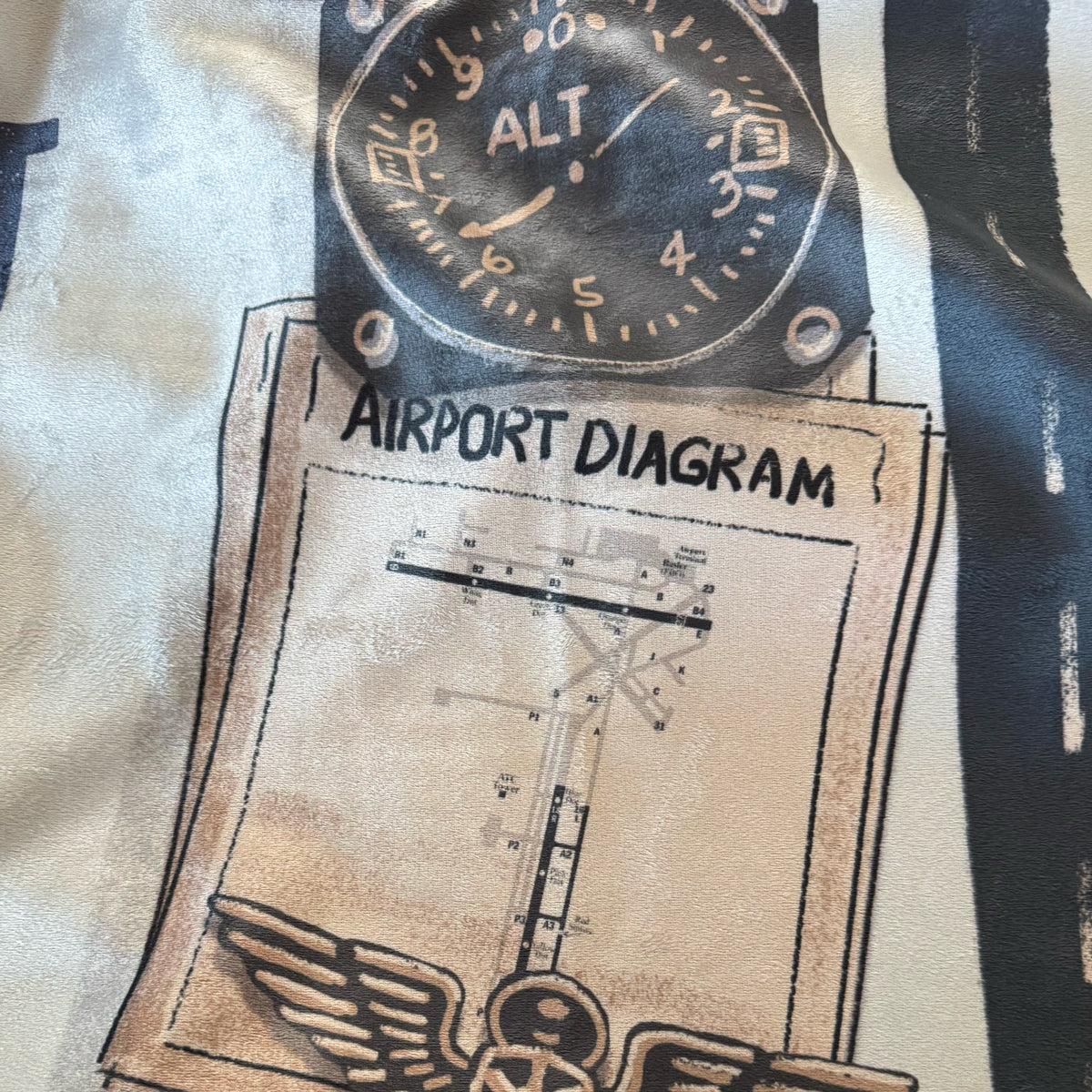 Close-up of a blanket with Oskosh KOSH airport diagram and altimeter design.