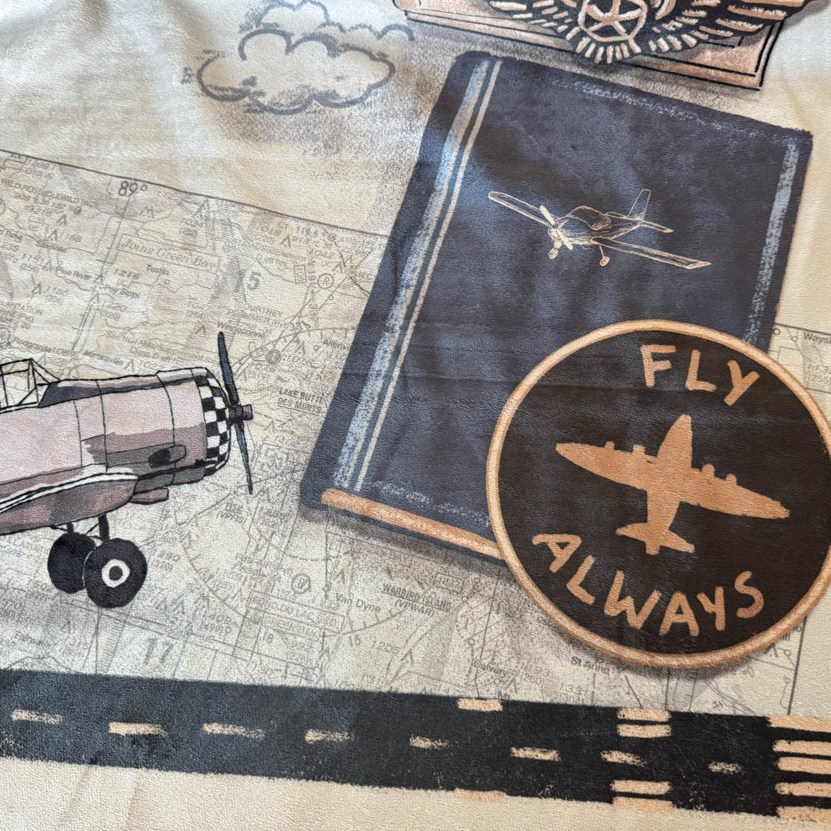 Blanket closeup of airplane book with 'Fly Always' patch on a map background