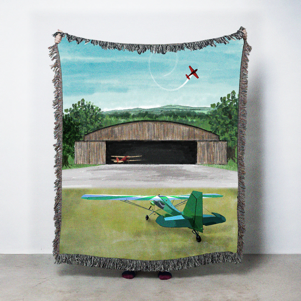 Woven blanket with an old airplane hangar in a hillside setting
