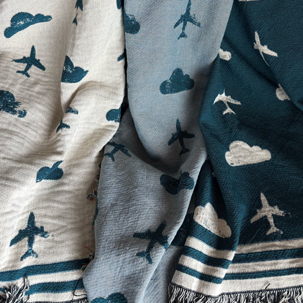 Three patterned travel blankets with airplane and cloud designs in blue and gray tones.