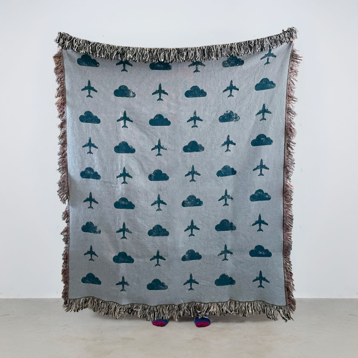 Travel blanket with airplane and cloud patterns on a light blue/gray background