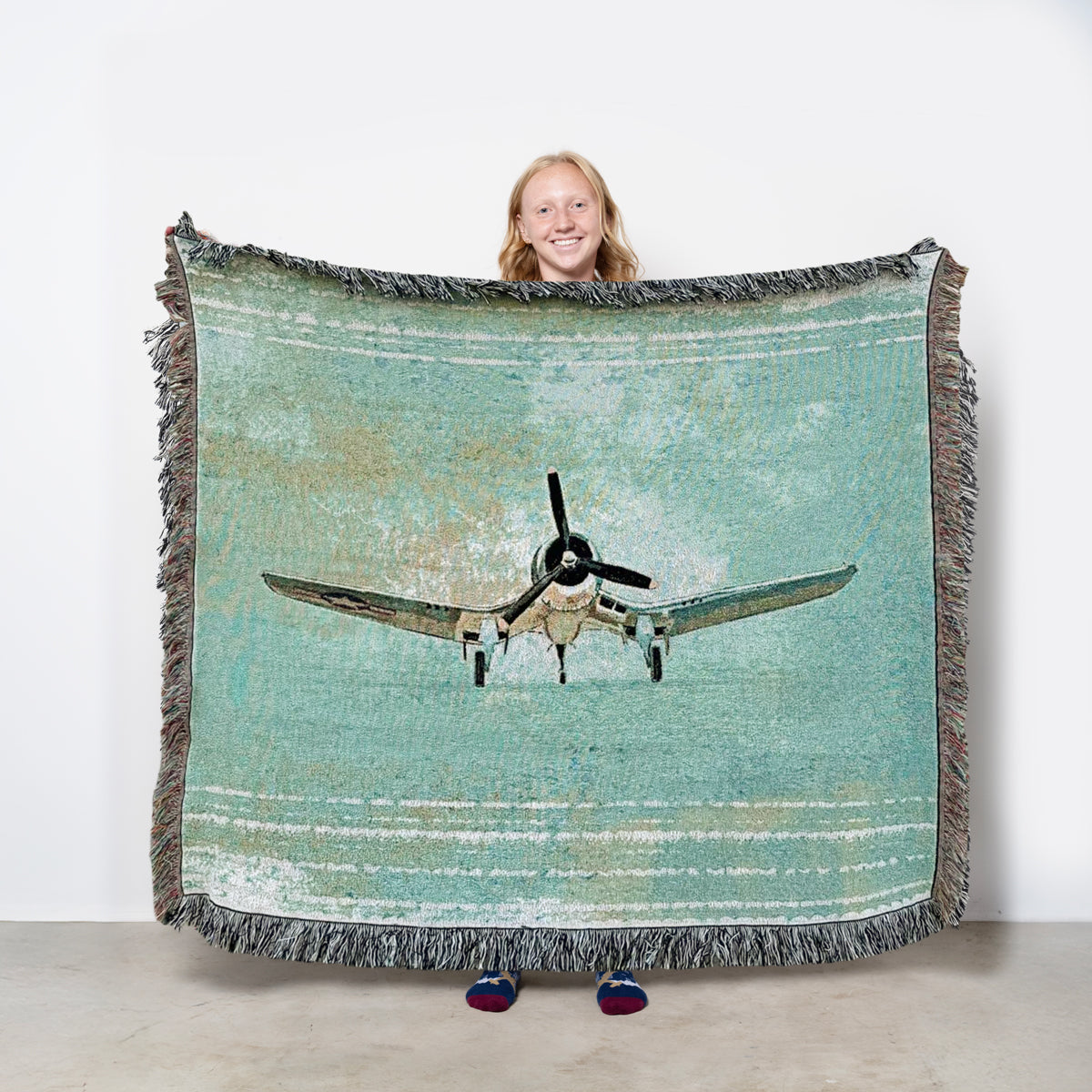 Woven blanket with a vintage Vought F4U Corsair airplane design on a green background
