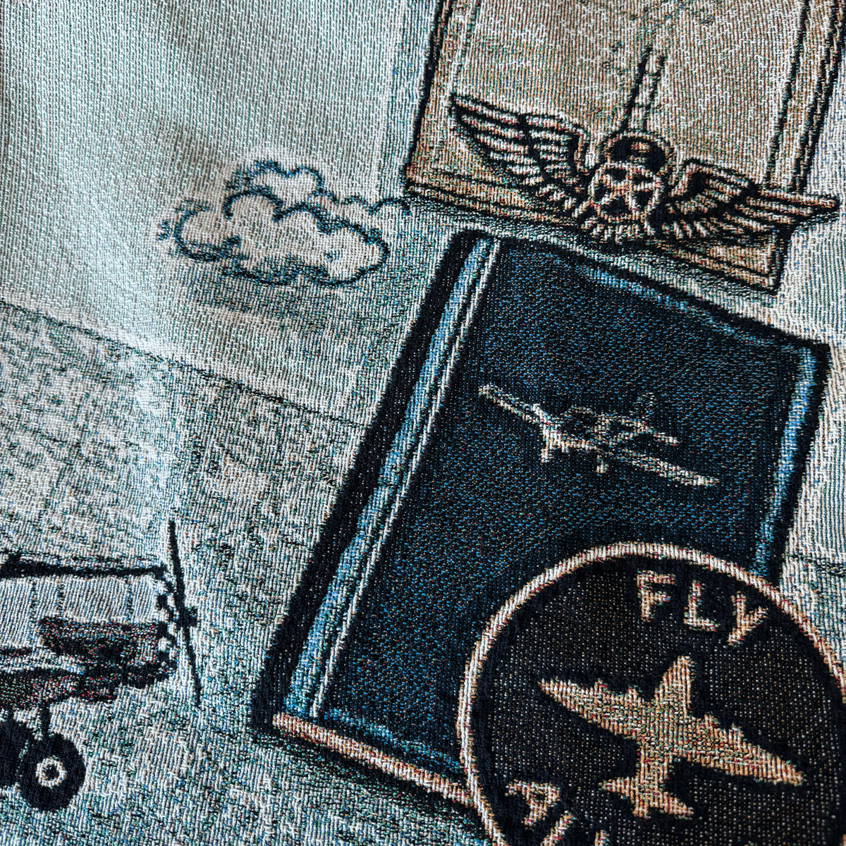 Woven blanket closeup  with airplane designs and 'FLY' text on a fabric background