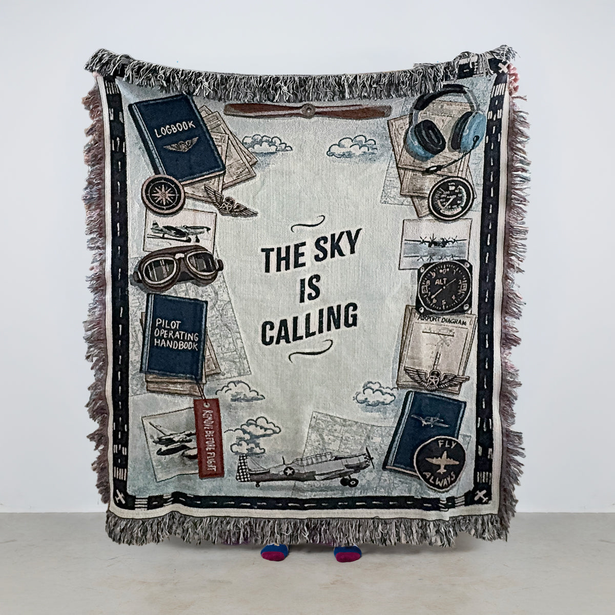Woven throw blanket with aviation-themed design and 'The Sky is Calling' text on a white background