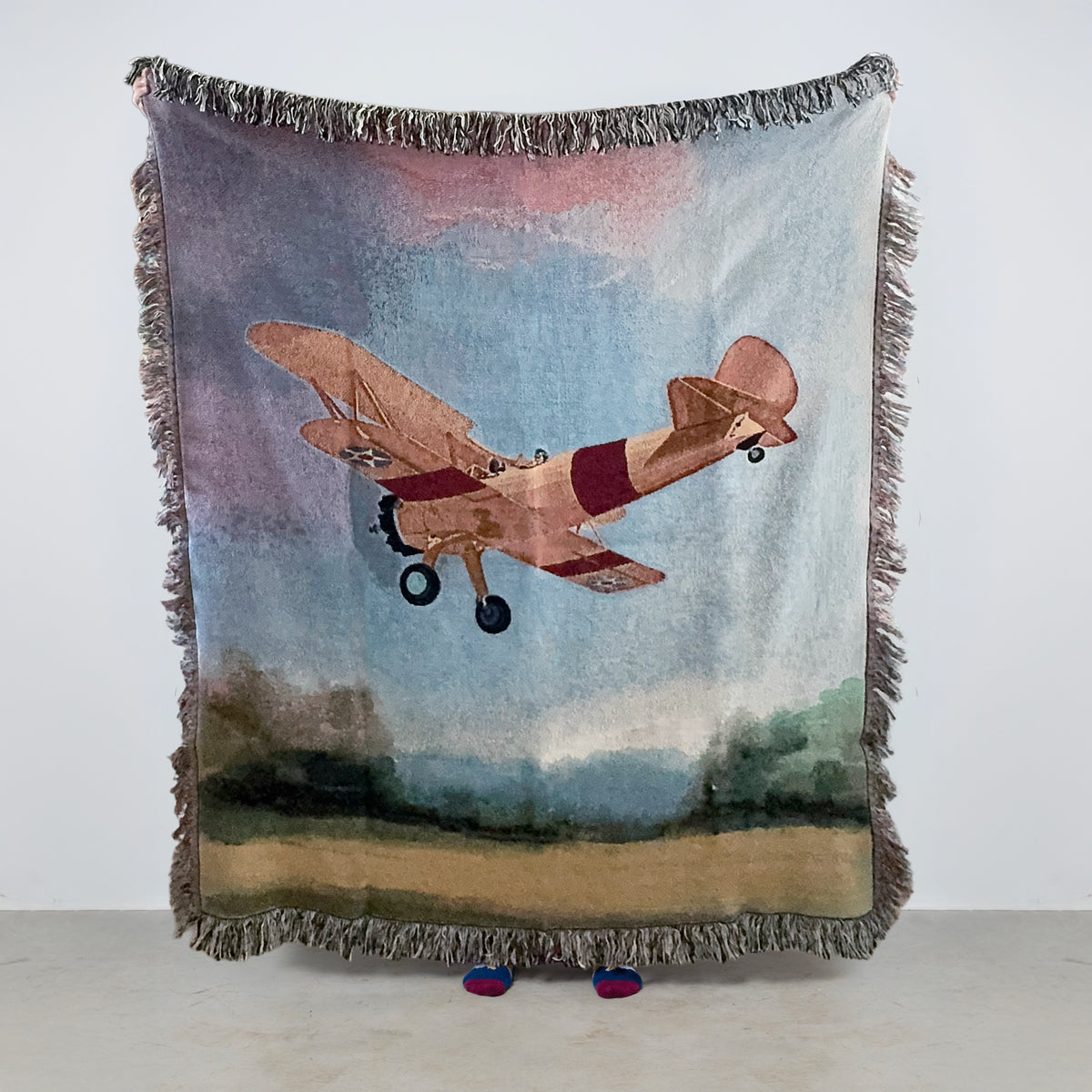 woven blanket with vintage biplane airplane flying over a field