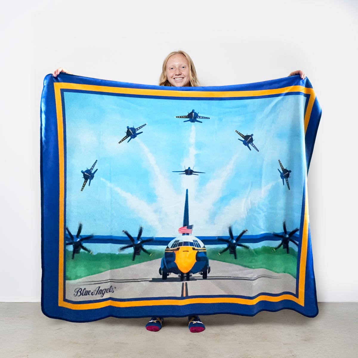 Officially licensed Blue Angels blanket featuring Fat Albert on the runway with six F/A-18 Super Hornets flying overhead in formation against an American flag backdrop.