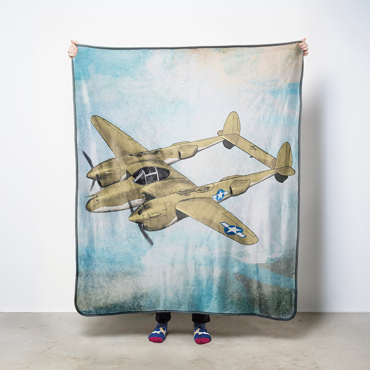 Fleece blanket with a vintage Lockheed P-38 Ligntning airplane illustration against a sky background
