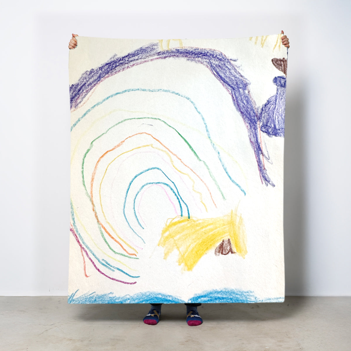 Person holding a large colorful drawing of a rainbow and a fish on a white wall. Add your own child's drawing.