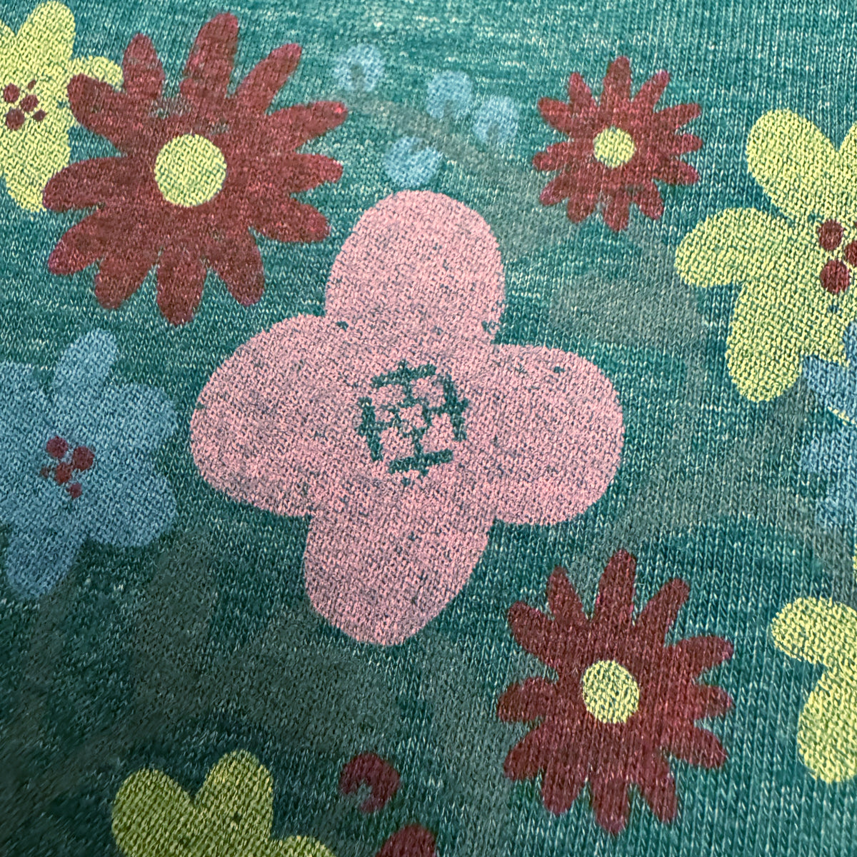 Floral patterned airplane t-shirt closeup with a pink flower in the center on a teal shirt