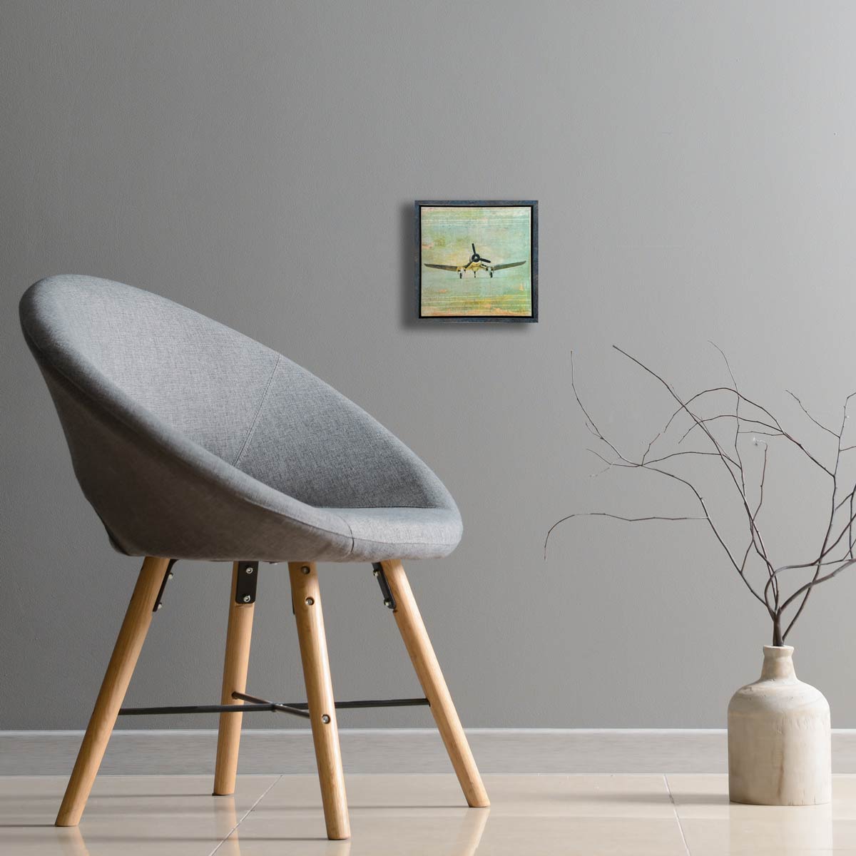 Gray chair with wooden legs in a room with a vase and framed corsair picture on the wall.