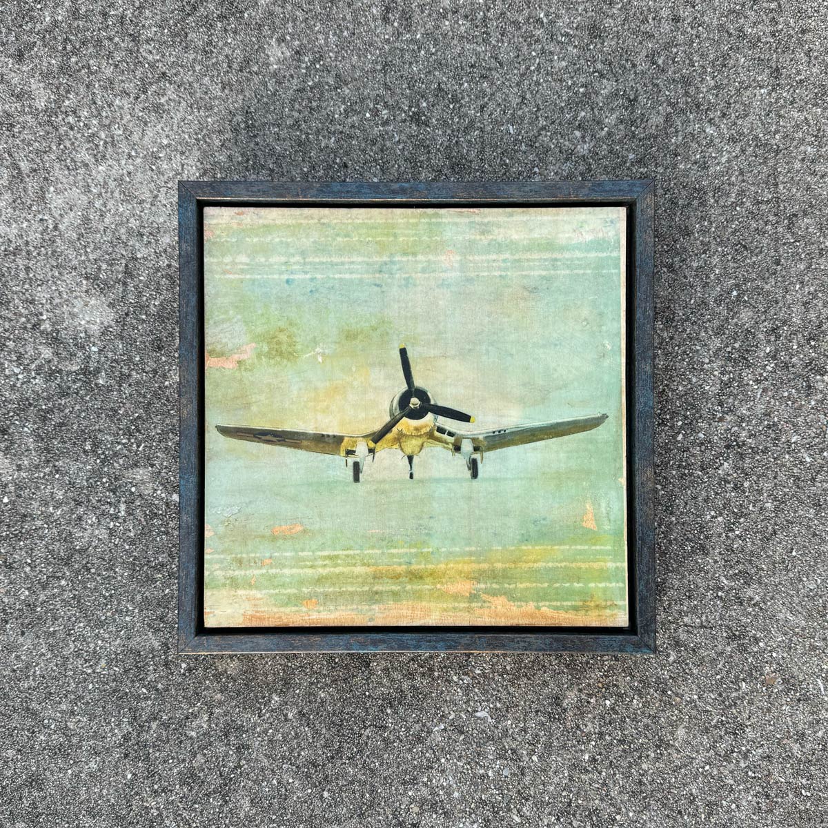Framed artwork of a vintage corsair airplane on a textured wall.