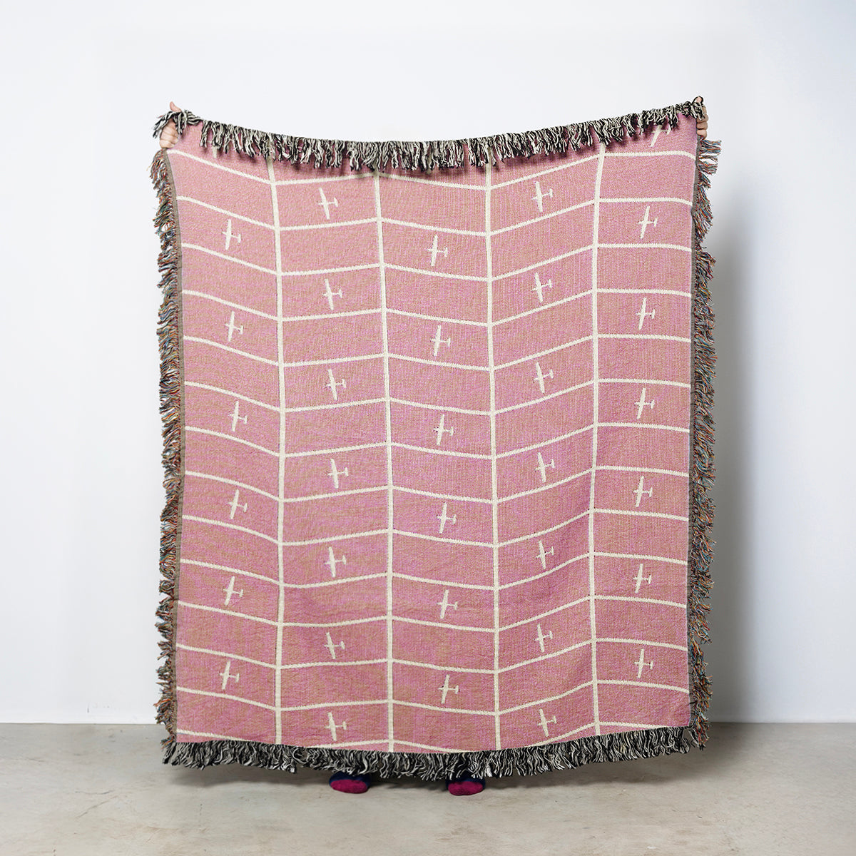 Pink blanket with white geometric airplane pattern and colorful fringe