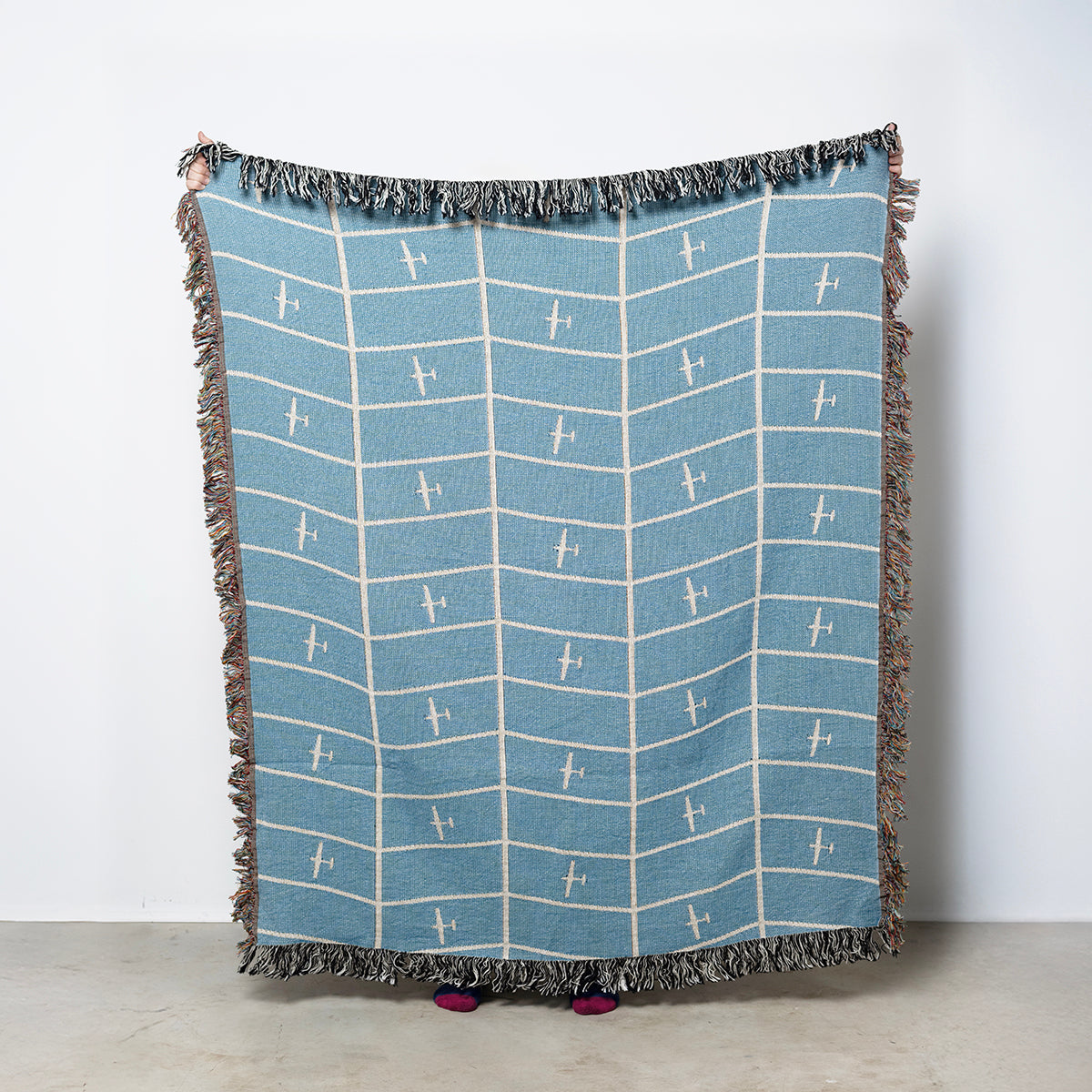 Blue and white patterned throw blanket with fringe on a light blue background