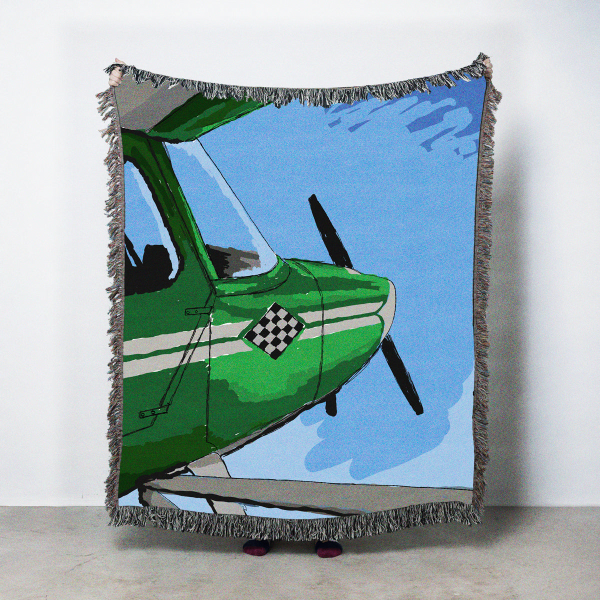 Woven blanket with a green airplane design on a blue sky background