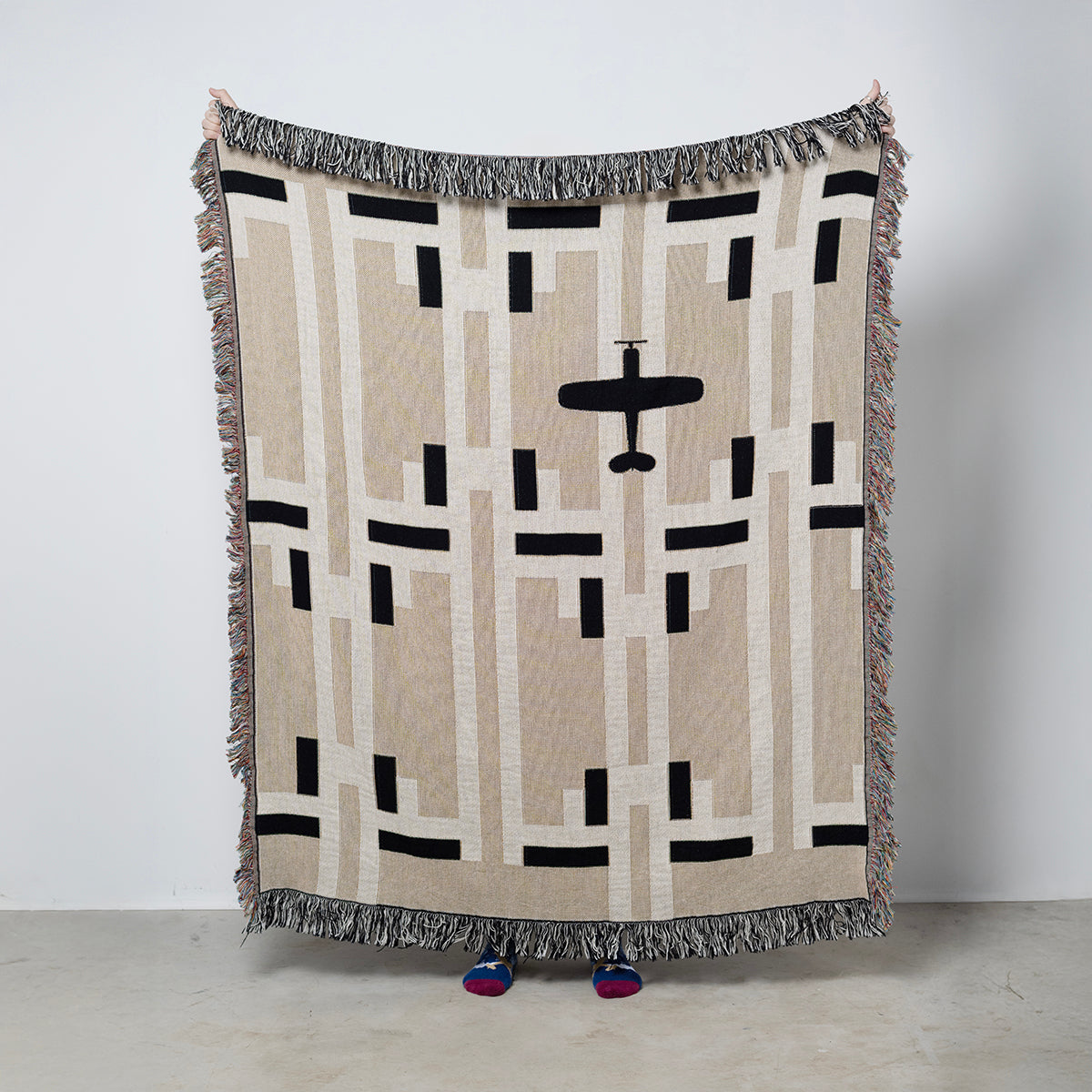 Woven blanket with an overhead view of airplane on a tan and cream geometric background