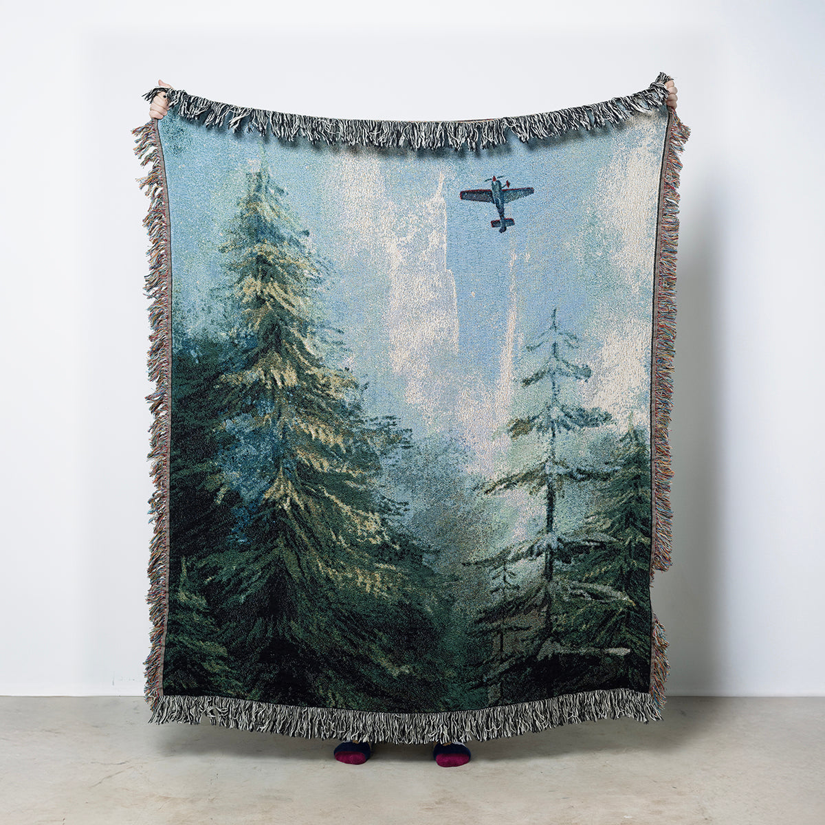 Woven blanket with a forest and airplane with northern lights