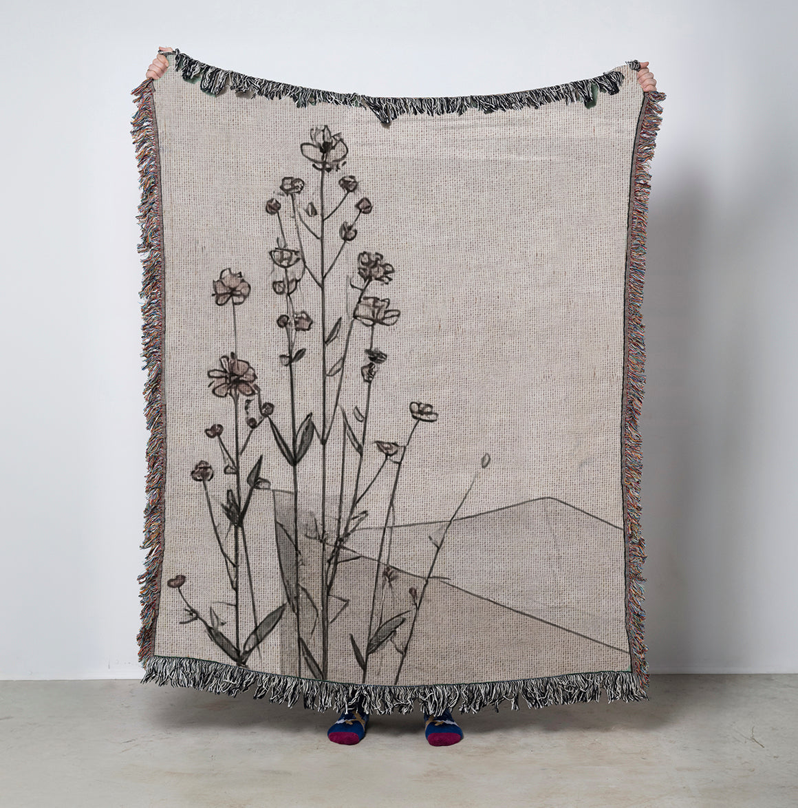 Woven blanket with floral design and abstract shapes on a plain background